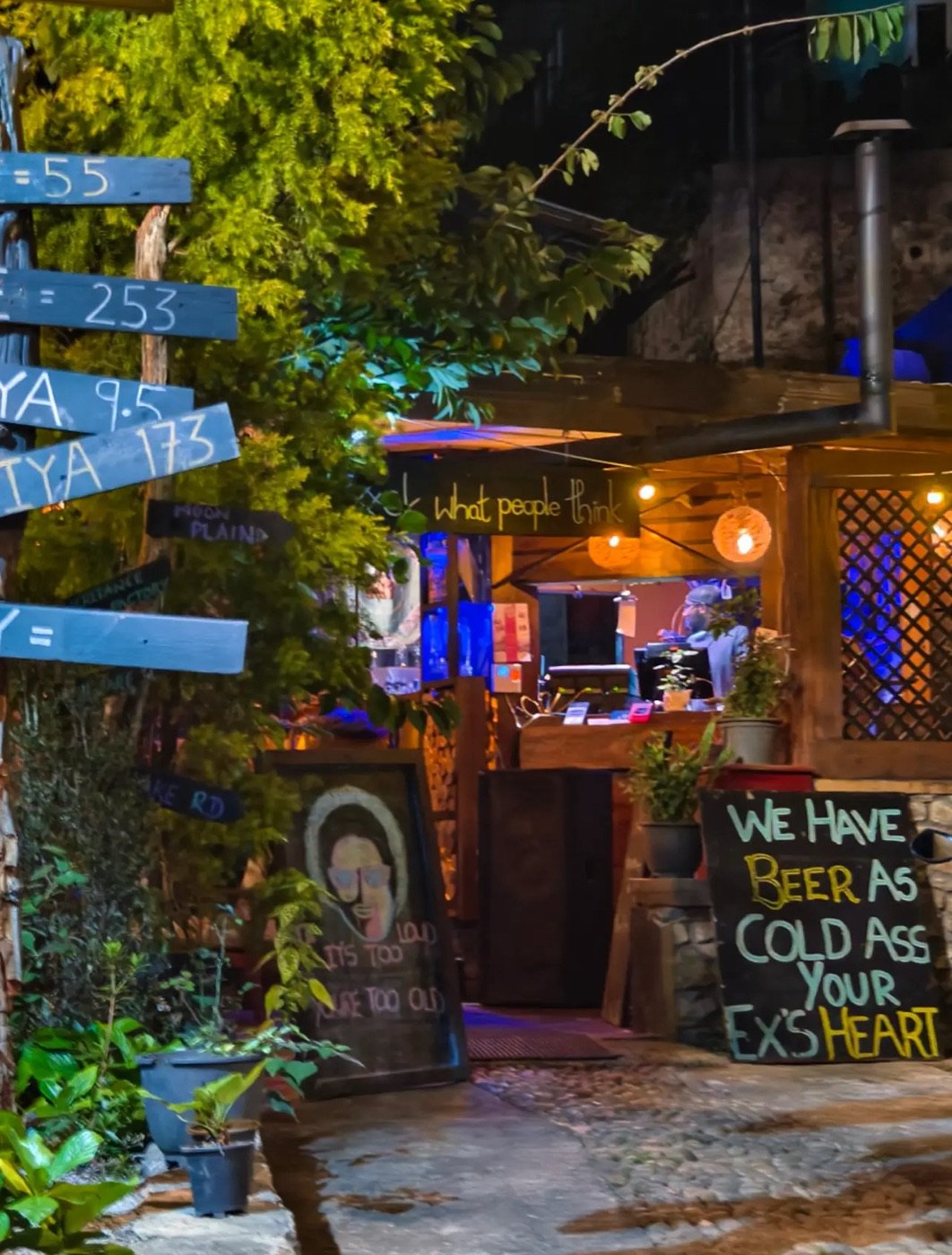 The Themparadu entrance at night, with signposts, warm lights and a chalkboard sign